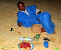 Mahmoud relaxes after a long battle with the Sahara (note propane burner, tea kettle, and raw camel meat!), Ben Amira, Mauritania, Africa